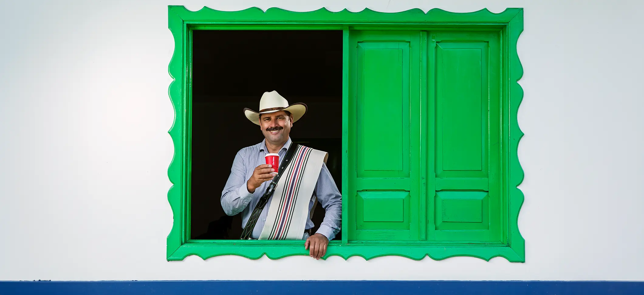 フアン・バルデスコーヒーの「私たちのブランド」セクションのヒーローイメージ：窓から覗く笑顔のコーヒー農家